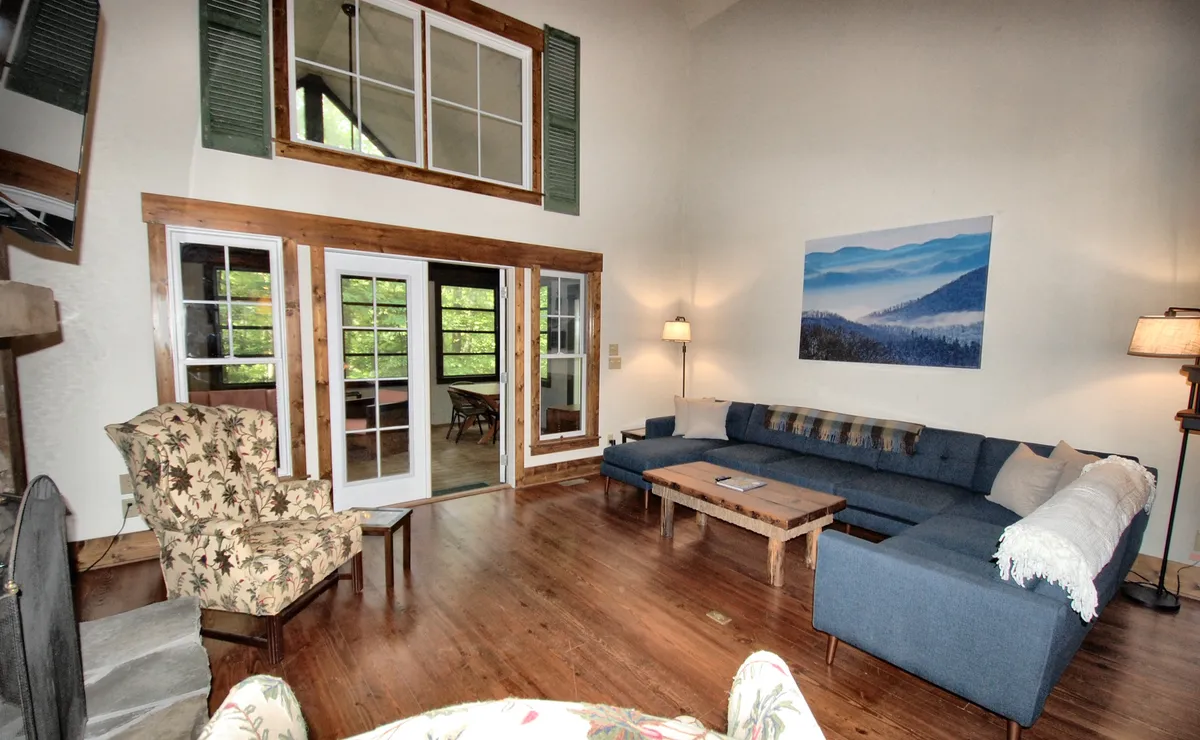 A cozy living room with a large sectional sofa, a floral armchair, expansive windows, and mountain-inspired artwork. The seating arrangement is ideal for group relaxation, conversation, or enjoying views, reinforcing the sense of warmth and togetherness.