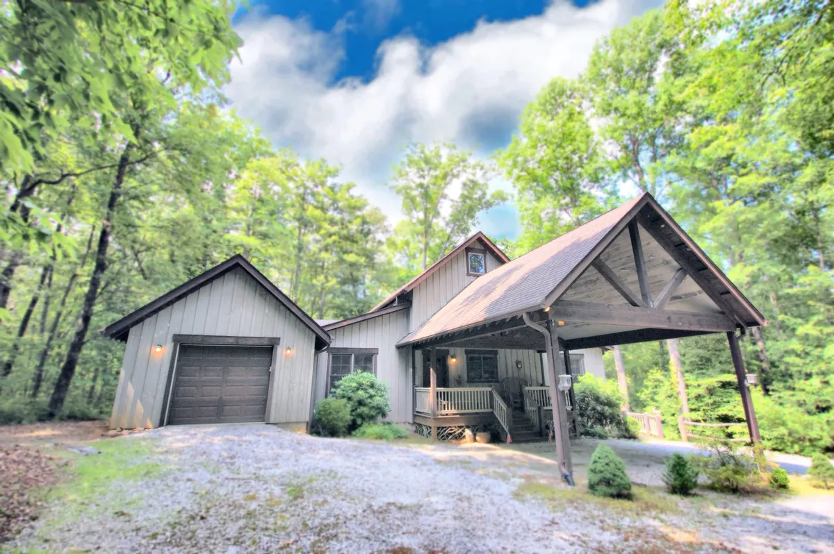 A wide view of the home's front porch with sturdy wooden beams, surrounded by a landscaped yard set against lush greenery. The inviting porch acts as a natural transition space between the comfort of the home and the wild outdoors, with plenty of room for family gatherings and outdoor relaxation. The open space and proximity to the woods suggest easy access to outdoor adventures.