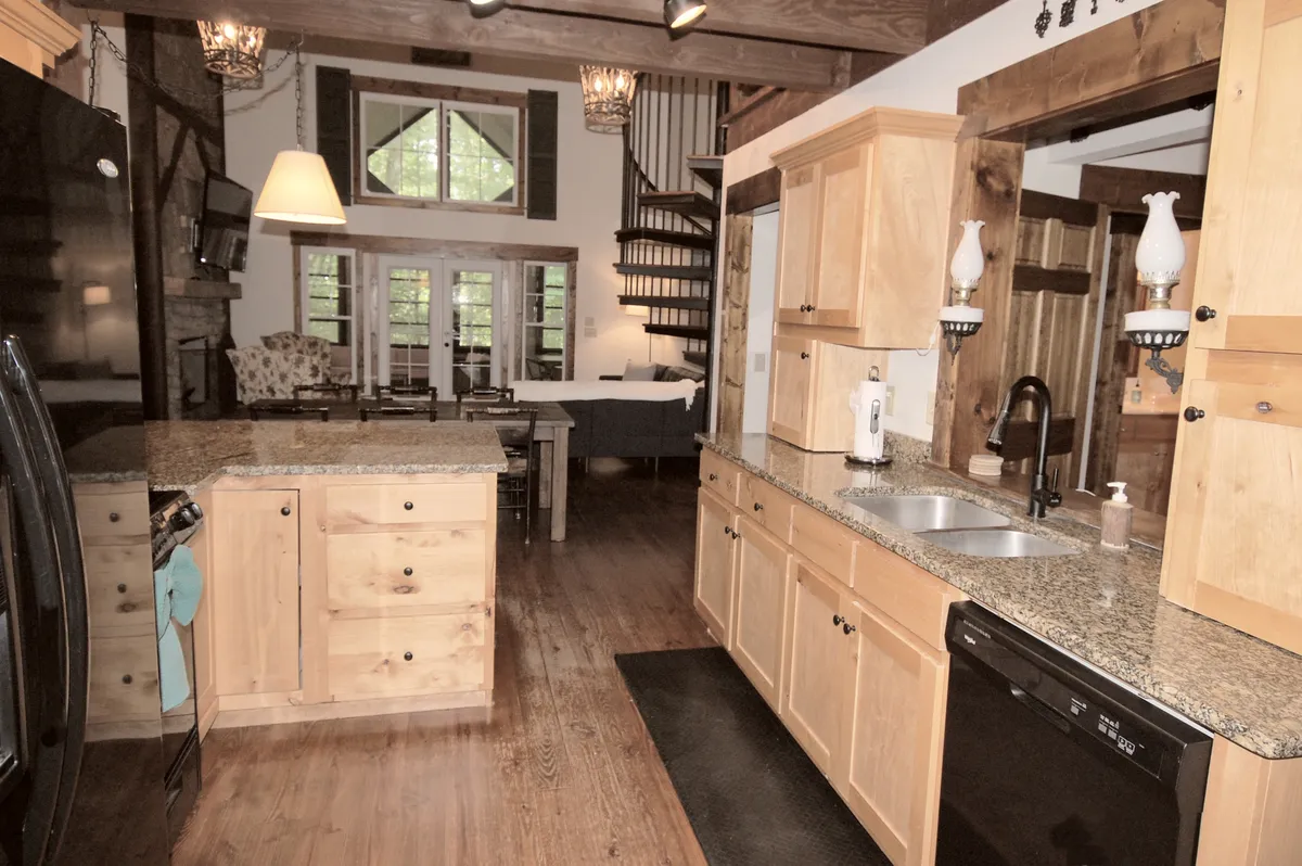 A spacious, open-plan kitchen and dining area featuring a prominent kitchen island, sleek modern appliances, an adjoining spiral staircase, a generous dining table, and large windows that fill the space with natural light. The arrangement invites socializing, cooking, and shared meals.