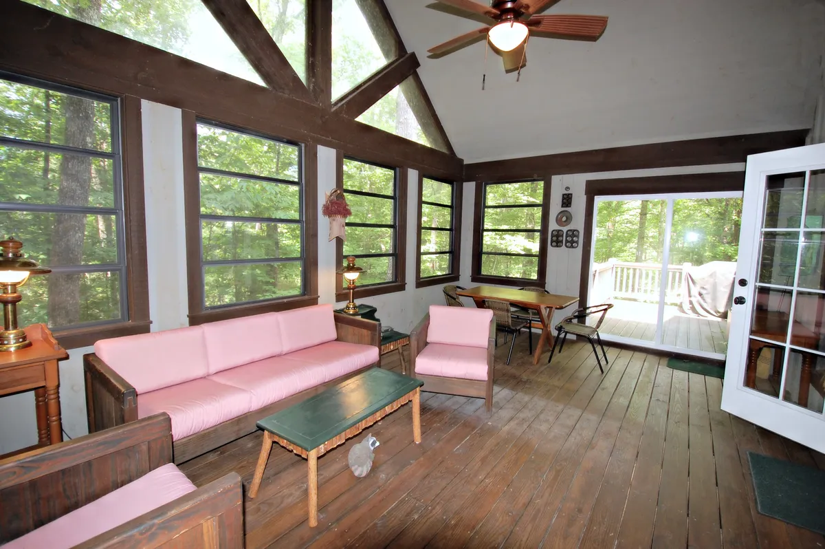 A cheerful living area with pink upholstered sofas, a green table, and large windows welcoming natural light. Wooden furniture and shelves suggest ample storage for books and games, and the relaxed, light-filled atmosphere hints at a space ideal for children to unwind or play.