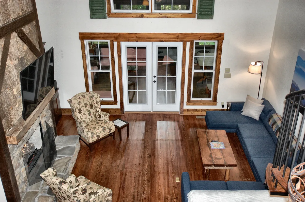 This scene features a welcoming living room anchored by a stone fireplace, surrounded by plush sofas and chairs. The large windows flood the room with light and offer views of the outdoors. The coffee table and armchair create a perfect nook for reading or board games, supporting both family bonding and cozy evenings.