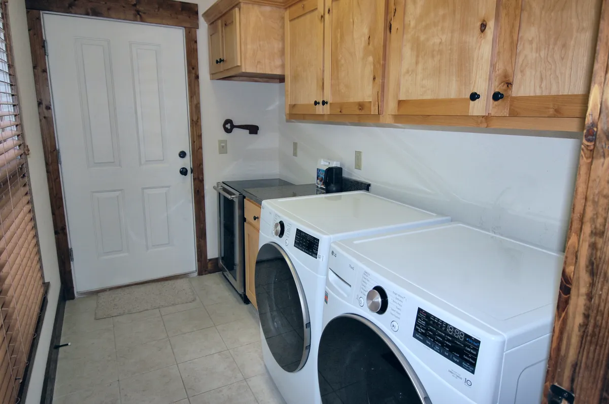A utility space with a washer and dryer, ample cabinetry, and a door that appears to lead directly outside. The room is sunlit and practical, indicating easy cleanup after outdoor adventures and convenient access to the outdoors.